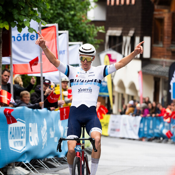 Ein Radfahrer jubelt mit erhobenen Armen beim Zieleinlauf. Zuschauer säumen die Strecke und applaudieren.