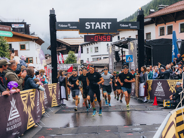 Athleten des Arlberger Wadlbeissers klettert über eine Holzrampe vor einer schönen Sommerkulisse mit Bergen und einem leicht bewölkten Himmel