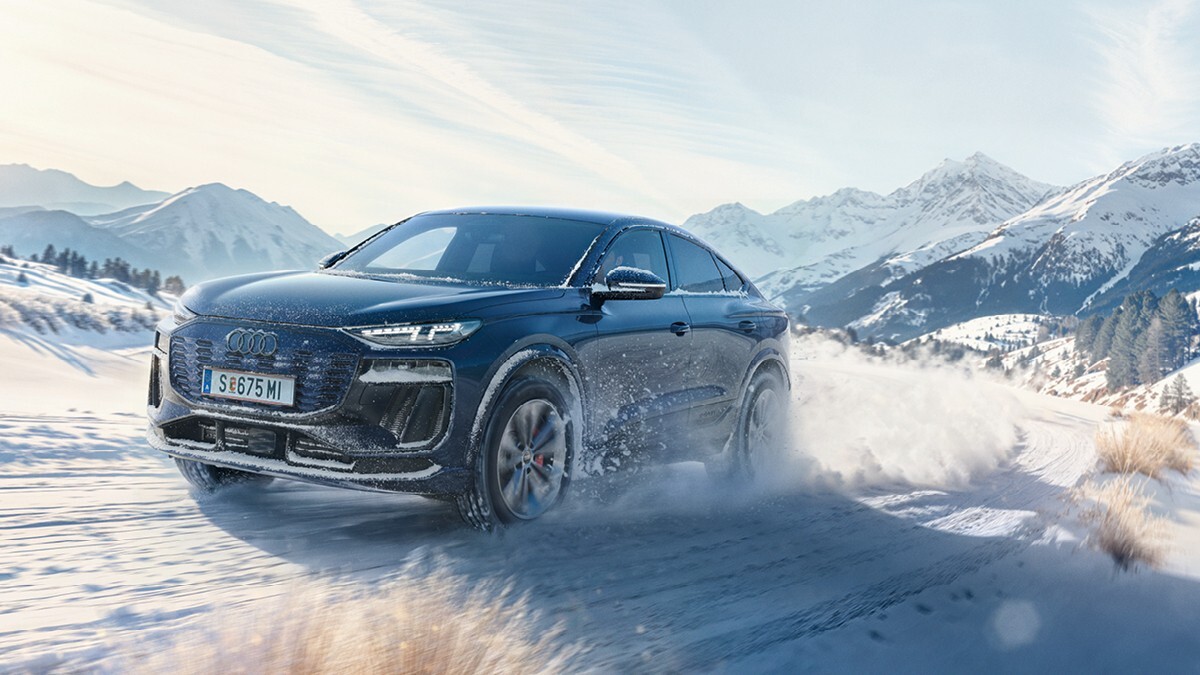 Audi electric car races through a snowy, alpine country road on a beautiful, slightly cloudy winter day.