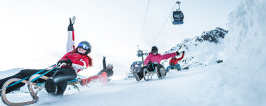 Rodelnde Wintersportler:innen auf Holzrodel unter der Nassereinbahn