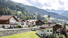 Flirsch on a mildly clouded summer day, with a great view on the parish church and the mountain range in the backdrop