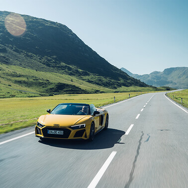 A yellow Audi R8 drives along a high alpine open road. In summer, when the weather is nice.