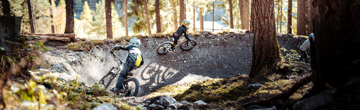 Three children riding the Seelenzoll Trail Park one after another, shot from behind in autumnal conditions.