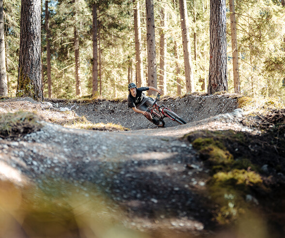 A mountain biker leaning into a sharp turn in autumnal conditions.