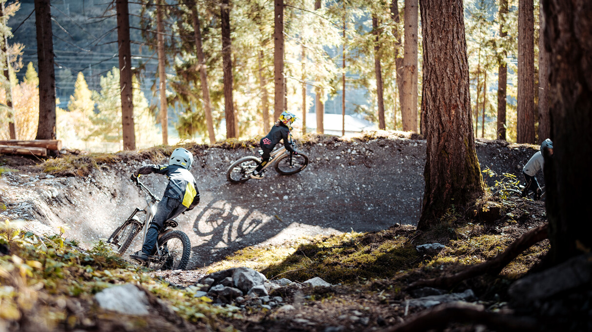 Drei Kinder fahren den Trailpark Seelenzoll hintereinander, Aufnahme von hinten bei herbstlichen Bedingungen.
