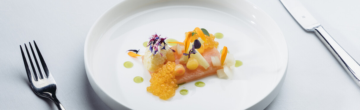 Lachsgericht mit Kaviar und Blüten auf weißem Teller.