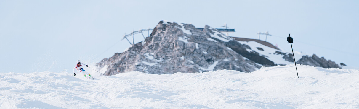 Skifahrer rast die buckelige Piste in St. Anton hinunter, Schindlergrat ist im Hintergrund zu sehen