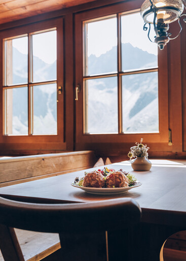 Knödel auf einem Tisch mit Aussicht durch ein Fenster der Darmstädter Hütte auf felsige Berge