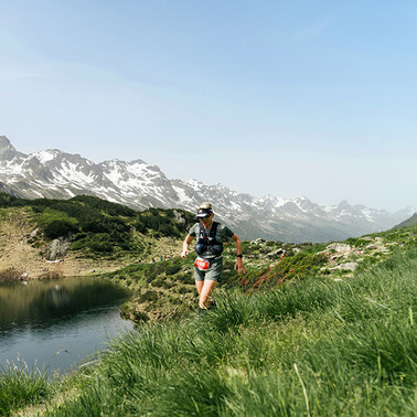 A runner passes a mountain lake, with a view of the mountainous panorama
