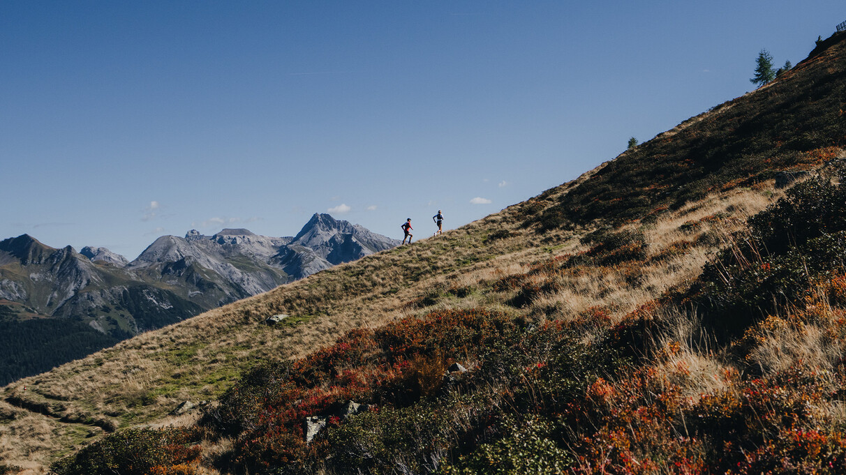 Zwei Trailrunner laufen einen Berg hinauf in einem schönem Bergpanorama