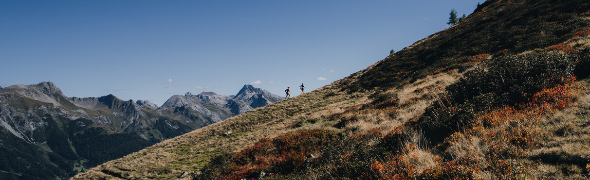 Two trail runners running up a mountain against a beautiful mountain backdrop