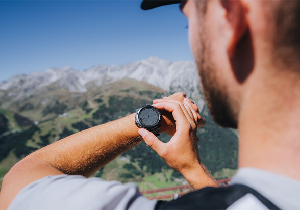 A trail runner checks his smartwatch against a summer mountain backdrop