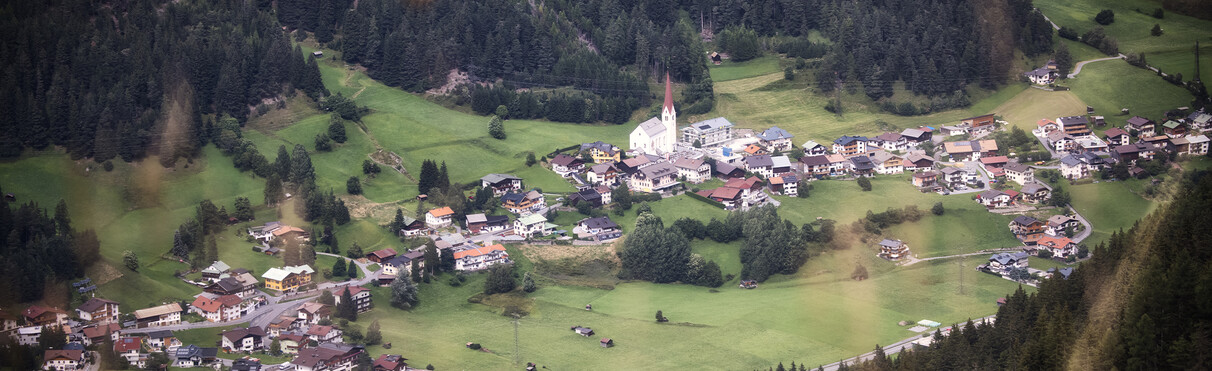 St. Jakob am Arlberg mit Kirche und umliegenden Häusern aus der Vogelperspektive.