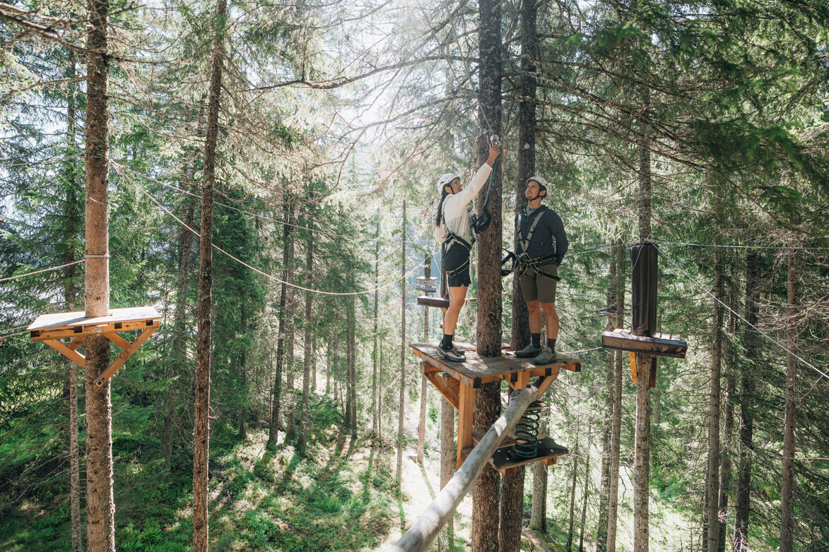 Vorbereitung auf das nächste Hindernis Zwei gesicherte Personen stehen auf einer Plattform im Waldseilgarten und bereiten sich auf das nächste Hindernis vor.