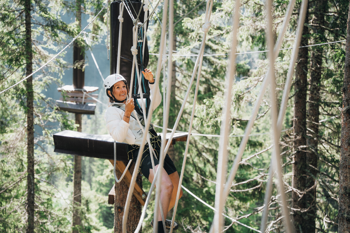 Seilhindernis im Waldseilgarten Gesicherte Person klettert durch ein Seilhindernis im Waldseilgarten zwischen den Bäumen.
