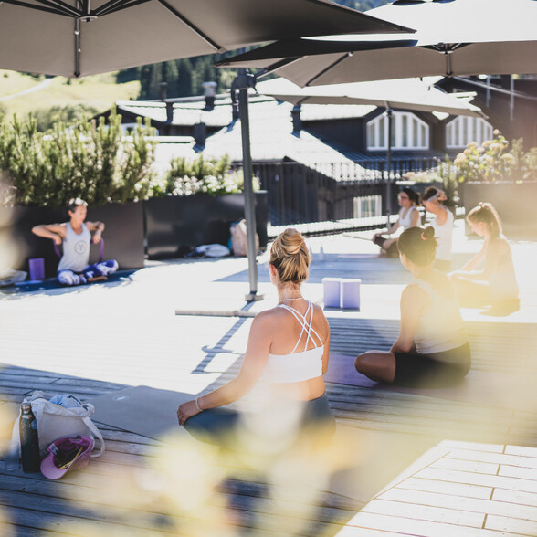 Gruppe von Menschen sitzt auf Yogamatten im Freien unter Sonnenschirmen und praktiziert Yoga