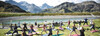 Yoga in St. Anton am Arlberg Gruppe von Menschen praktiziert Yoga auf bunten Matten auf einer Wiese vor einem Bergsee mit dem Patteriol im Hintergrund