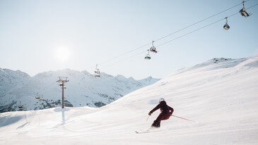 Lifts and Slopes Skier descending a snowy slope with chairlifts and snow-covered mountains in the background