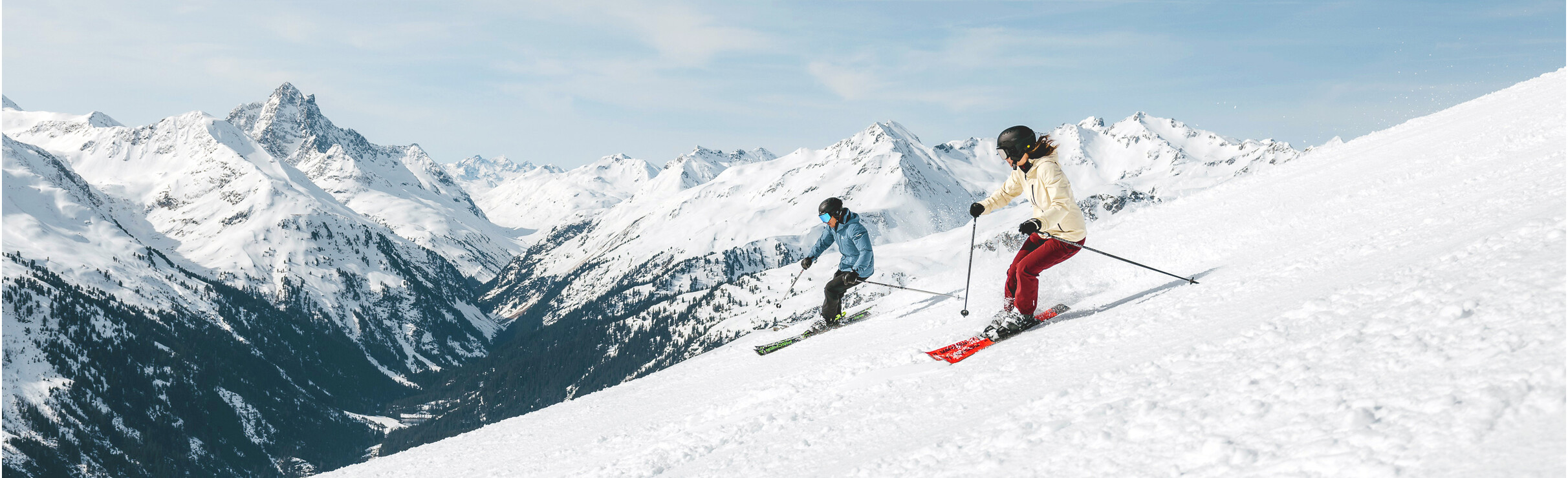 Ski Arlberg Twee skiërs dalen een besneeuwde berghelling af met besneeuwde bergtoppen op de achtergrond