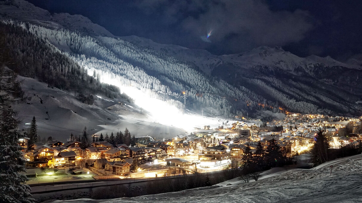 Dronefootage of a snowy, wintery St. Anton am Arlberg by night. Surrounded by a snow-covered mountain range.