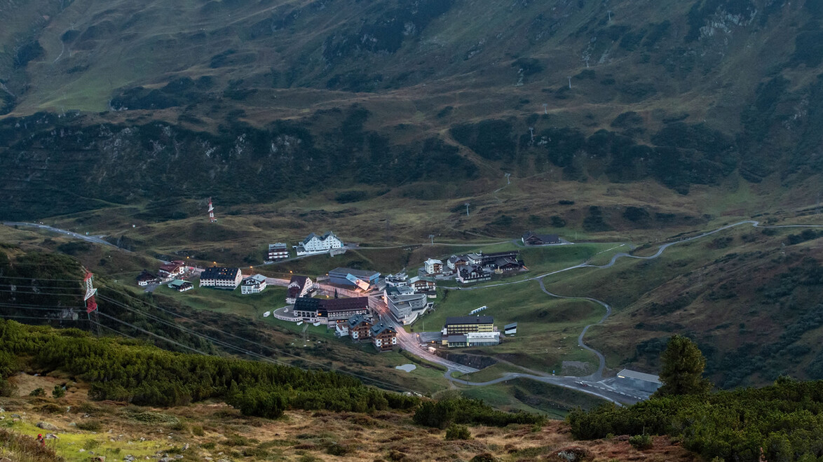 Blick auf St. Christoph am Arlberg inmitten grüner Almen und Berglandschaft bei Tageslicht. / View of St. Christoph am Arlberg surrounded by green alpine meadows and mountain landscape during daylight.