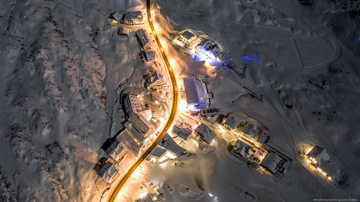 Luftaufnahme von St. Christoph bei Nacht, beleuchtete Straßen und Gebäude im Schnee. / Aerial night view of St. Christoph with illuminated streets and buildings in the snow.