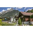 Typische Tiroler Häuser vor steilem bewaldetem Berg im Sommer. / Typical Tyrolean houses in front of forested mountain slope in summer.