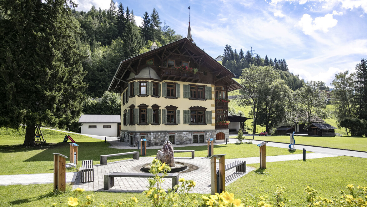 Sommerliche Parkanlage mit Spielbereich vor historischem Gebäude. / Summer park area with playground in front of historic building.
