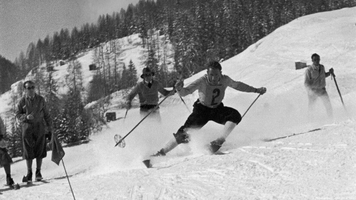 Gruppe von Skifahrern fährt sportlich den Hang hinunter im klassischen Stil. / Group of skiers descend the slope in athletic, classic style.