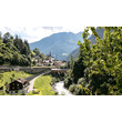 Strengen im Sommer mit grünen Wiesen, Fluss und Kirche vor alpiner Kulisse. / Summer in Strengen with green meadows, river, and church against alpine backdrop.