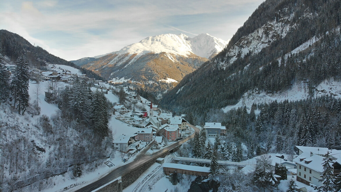 Strengen im verschneiten Tal mit Blick auf die leuchtende Bergspitze bei Sonnenuntergang. / Strengen in a snowy valley with glowing mountain peak at sunset.