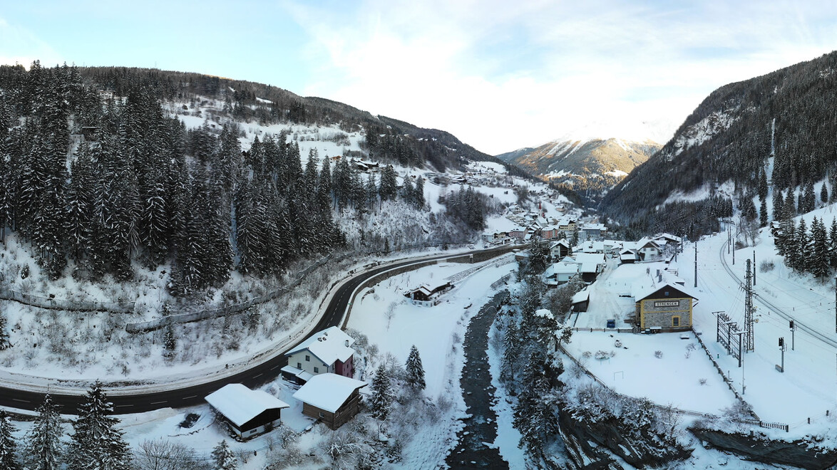 Strengen im Winter mit verschneiten Häusern entlang des Flusses, umgeben von Wäldern und Bergen. / Winter view of Strengen with snow-covered houses by the river, surrounded by forest and mountains.