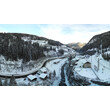 Strengen im Winter mit verschneiten Häusern entlang des Flusses, umgeben von Wäldern und Bergen. / Winter view of Strengen with snow-covered houses by the river, surrounded by forest and mountains.