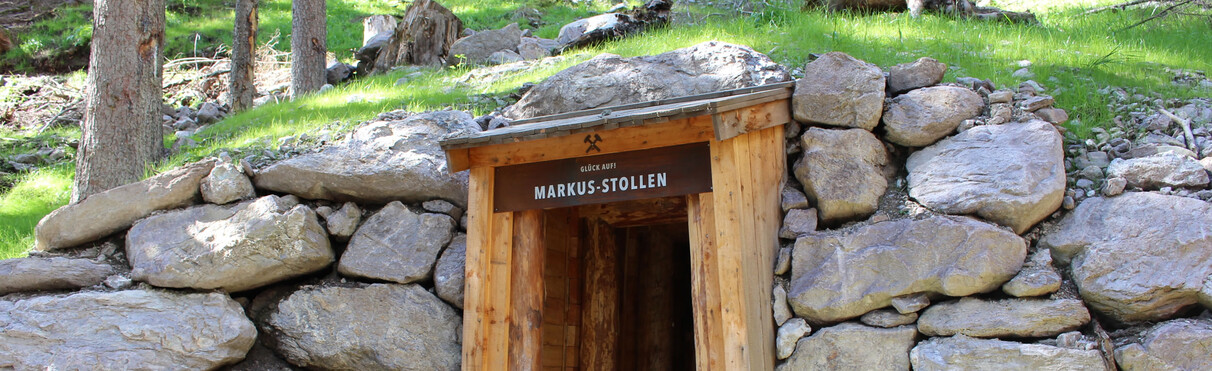 Entrance to the Markus-Stollen mine near St. Anton am Arlberg – historic timber-framed tunnel surrounded by rocks and forest greenery.