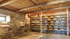 Cheese cellar with wooden shelves full of wheels, hanging bacon and dim lighting