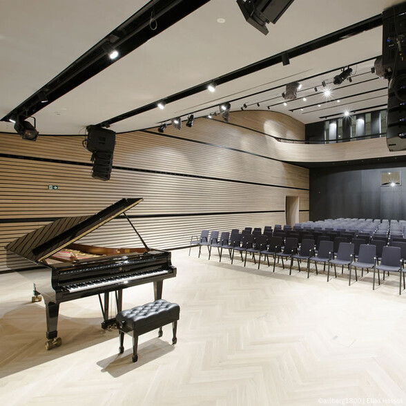 Modern concert hall with a black grand piano in the foreground and rows of chairs behind – venue in the arlberg1800 resort.