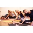 Drei Frauen dehnen sich seitlich im Sitzen auf Yogamatten. — Three women perform side stretches while seated on yoga mats.