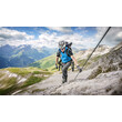 Ein Bergsteiger klettert mit Helm und Klettersteigset an einem Drahtseil entlang auf einem felsigen Pfad mit Panoramaausblick. / A climber with helmet and via ferrata gear ascends a rocky trail secured by a steel rope, with panoramic mountain views.