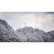 Ein Gipfelkreuz steht auf einem felsigen Berggrat unter bewölktem Himmel. / A summit cross stands on a rocky mountain ridge under a cloudy sky.
