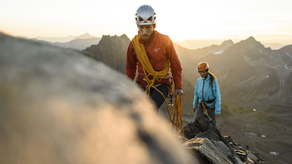 Zwei Kletterer auf einem schmalen Felsgrat bei Sonnenaufgang mit Seilsicherung. / Two climbers on a narrow rock ridge at sunrise, secured with rope.