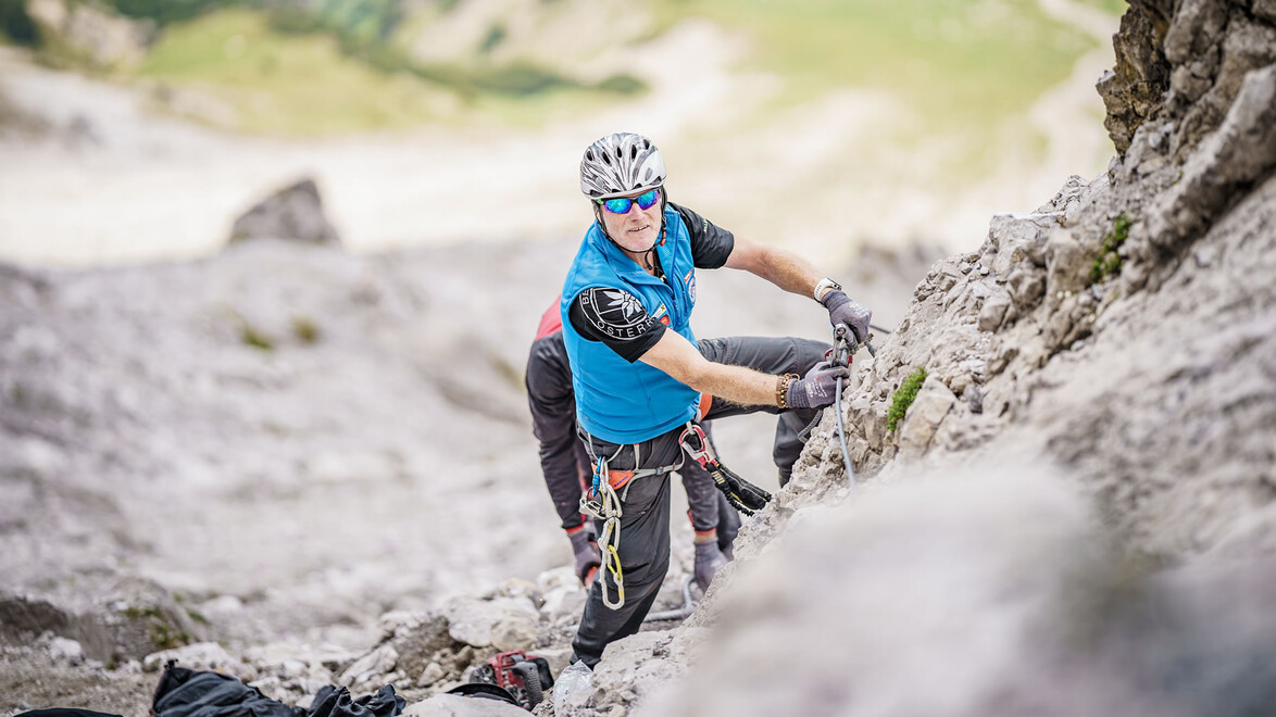Ein Kletterer sichert sich an einem Drahtseil in einer steilen Felswand beim Aufstieg. / A climber secures to a steel rope on a steep rock face during ascent.