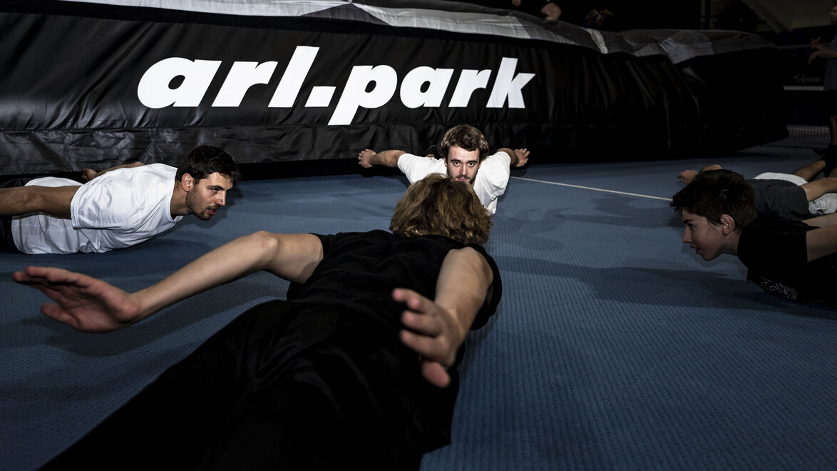 Mehrere junge Sportler wärmen sich gemeinsam auf einer blauen Matte im arl.park auf. / Several young athletes warm up together on a blue mat in the arl.park.