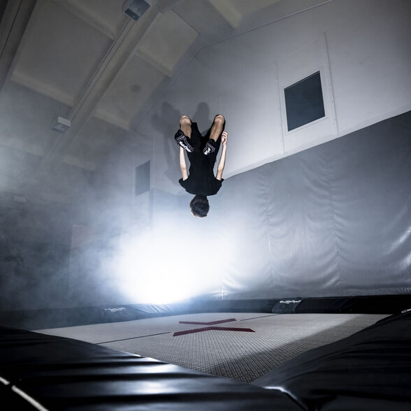 Young person doing a backflip on trampoline with fog and light effects in the background.
