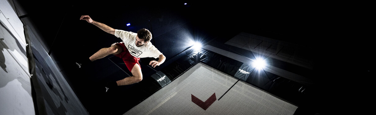  Teenager jumps high on trampoline performing a backflip under indoor lights.