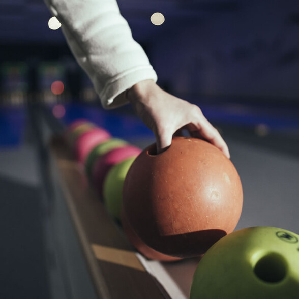 Hand greift nach orangener Kegelkugel, weitere Kugeln daneben.