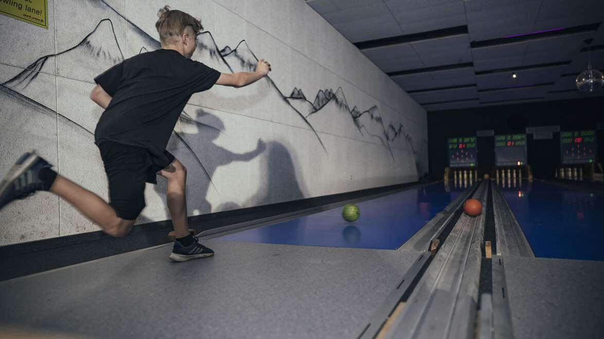 Kind beim Kegeln in dynamischer Bewegung, bunte Kugeln rollen auf die Bahn / Child bowling in dynamic motion, colorful balls rolling down the lane