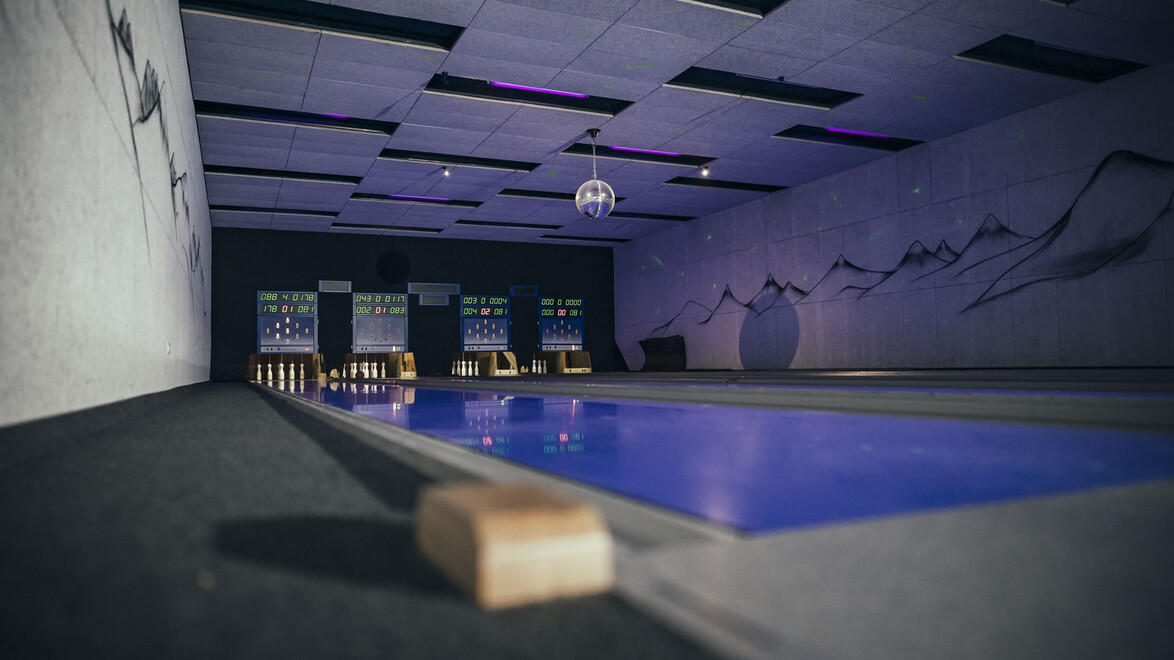 Leere Kegelbahn mit stilvoller Beleuchtung und vier Bahnen im Hintergrund / Empty bowling alley with stylish lighting and four lanes in the background