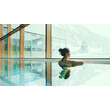 Eine Frau genießt den Blick auf verschneite Berge aus dem warmen Innenbecken / A woman enjoys the view of snowy mountains from the warm indoor pool