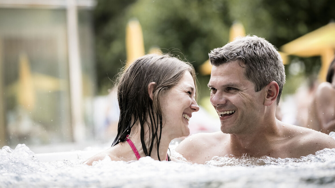 Ein Paar entspannt sich gemeinsam im sprudelnden Außen-Whirlpool / A couple relaxes together in the bubbling outdoor whirlpool