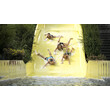 Vier Kinder rutschen lachend nebeneinander auf einer gelben Wasserbahn ins Becken / Four children slide down a yellow waterslide together, laughing and splashing into the pool
